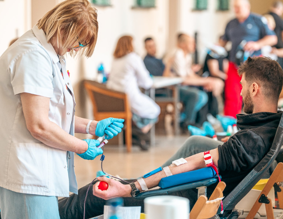 Na zdjęciu kobieta pobierająca krew, w tle czekający ludzie