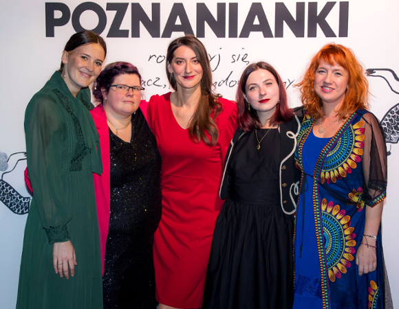 Na zdjęciu pięć uśmiechniętych kobiet, pozujących na ściance