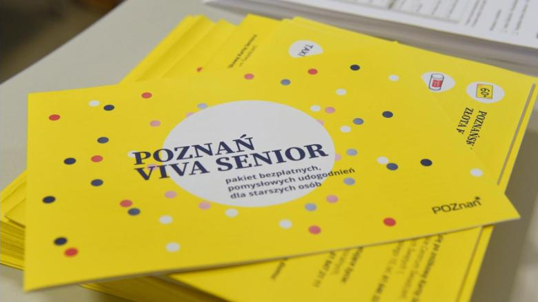 Zdjęcie przedstawia stos materiałów informacyjnych. Ich okładka to żółta kartka w kolorowe kropki, na niej białe koło i napis: Poznań Viva Senior