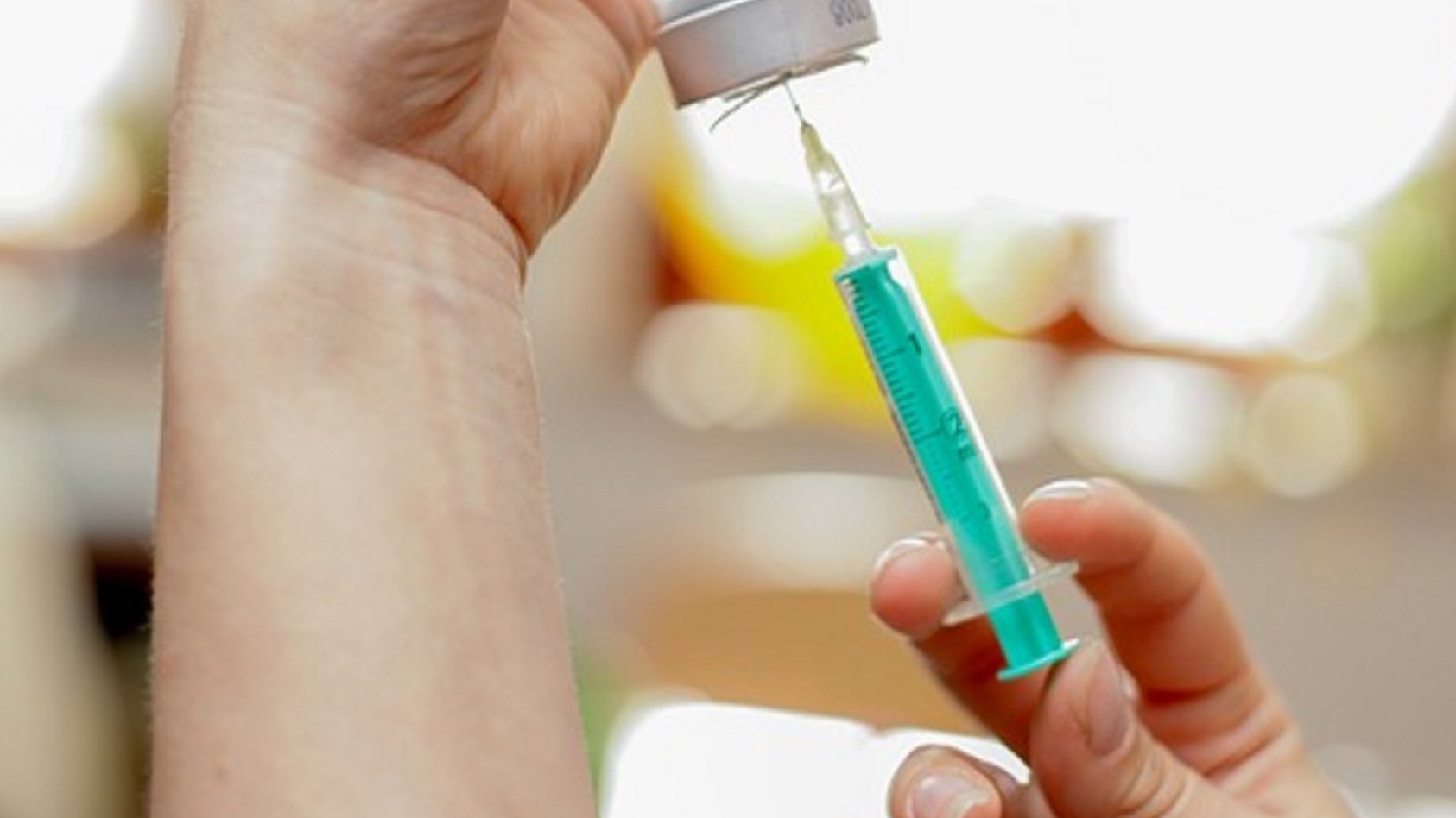 Na zdjęciu widać dwie dłonie osoby, która przygotowuje szczepionkę, w centrum zdjęcia strzykawka - grafika artykułu