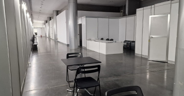 Na zdjęciu wnętrze punktu szczepień, widać stół z dwoma krzesłami, długi korytarz i punkt rejestracji