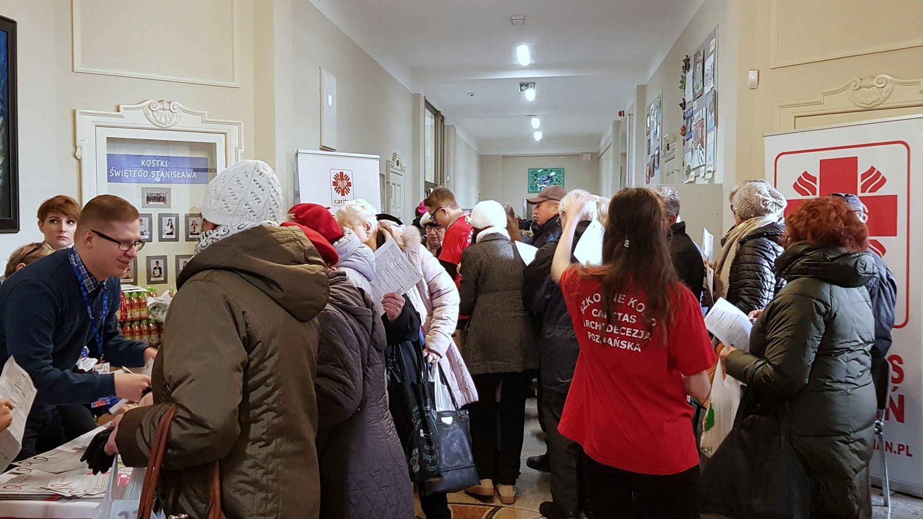 zdjęcie przedstawia tłum osób oczekujących w kolejce do rejestracji w budynku szkoły - grafika artykułu