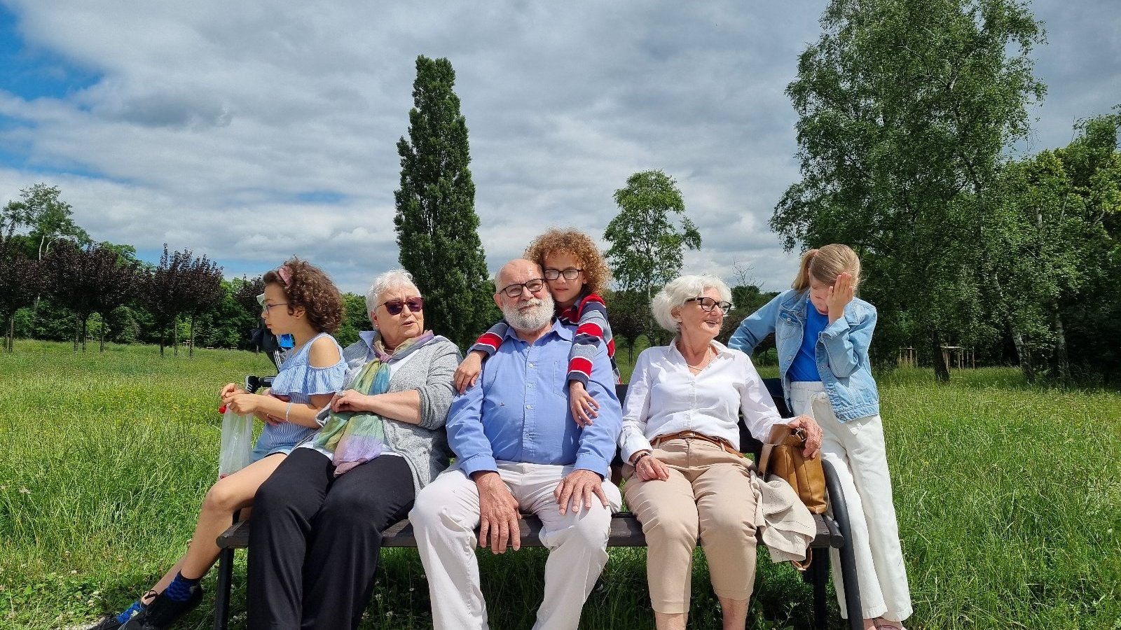 zdjęcie grupy dzieci i seniorów bohaterów kampanii społecznej na rzecz rodzinnej pieczy zastępczej. seniorzy siedza na ławce, dzieci przytlają sie do nich.