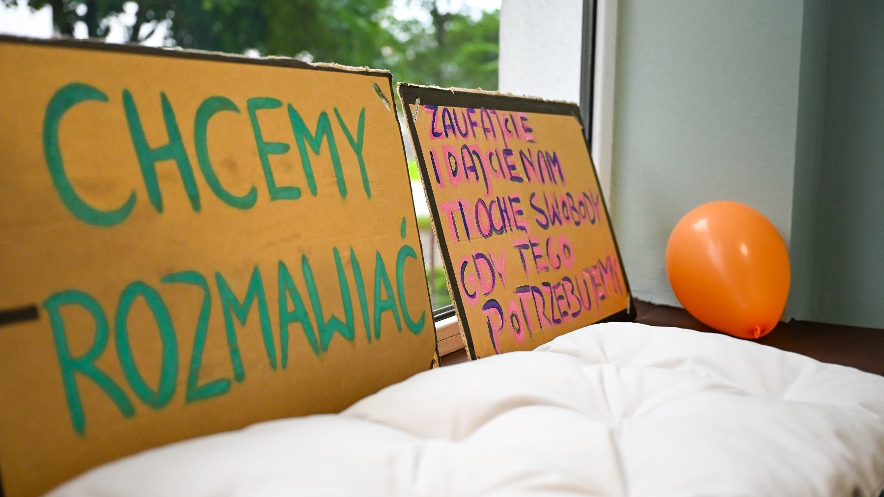 Na zdjęciu parapet, na nim poduszki i kartony z napisami: chcemy rozmawiać, zaufajcie nam
