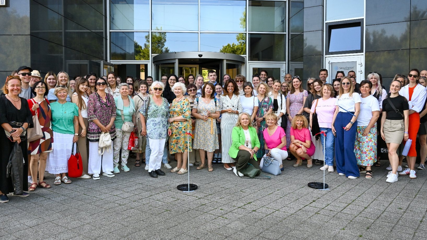 Na zdjęciu duża grupa ludzi przed szklaną fasadą biurowca, pozują do zdjęcia