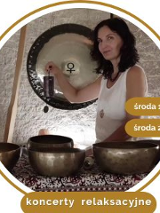 Kobieta w białej bluzce siedzi na dywanie. Przed nią stoją misy i gongi do grania.