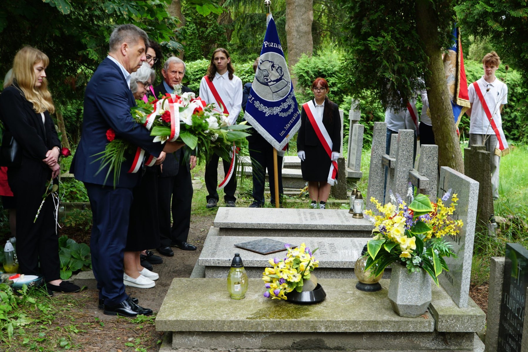 Uroczysta inauguracja XVIII edycji akcji "Światełko dla Czerwca '56" odbyła się na poznańskim cmentarzu parafii pw. Bożego Ciała przy ul. Bluszczowej/ fot. Muzeum Powstania Poznańskiego - Czerwiec 1956 Zdjęcie przedstawia grupę młodych ludzi oraz kilka osób dorosłych stojących przed grobem. Na grobie leżą kwiaty i stoją znicze. Młodzi ludzie trzymają w rękach róże.