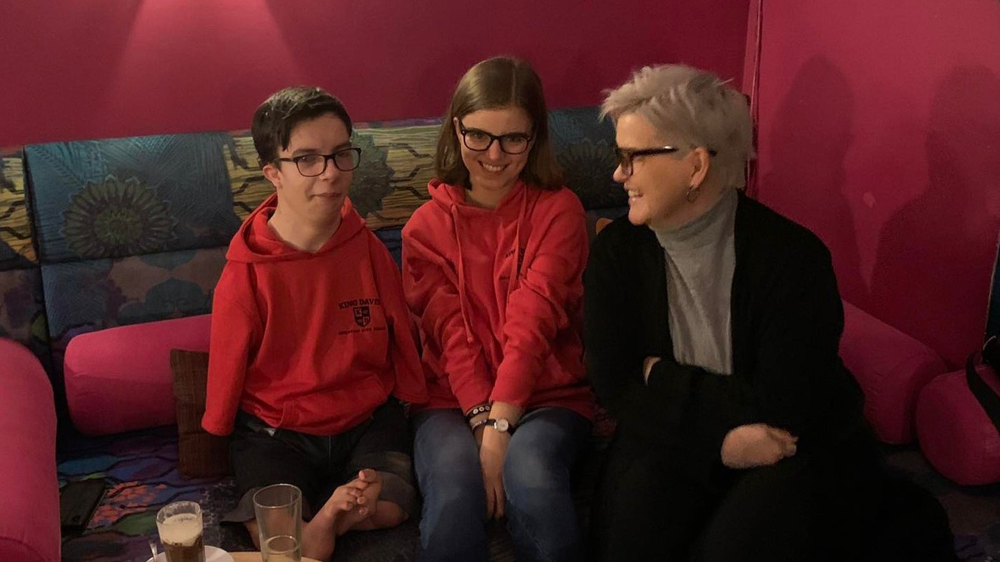 w roku sali kawiarni, na tle bordowych ścian siedzą Miłosz i Gosia oraz Agnieszka Maciejewska z Urzędu Miasta Poznania, uśmiechają się do siebie, przed nimi na stolikach kawa i ciasto - grafika artykułu