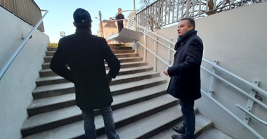 Na schodach w przejściu podziemnym stoja wicepezydent Poznania Mariusz Wiśniewski i drugi mężczyna, rozmawiają, w szczytu schodów na specjalnej poręcy zamontowana platforma dla osób ze szczególnymi potrzebami