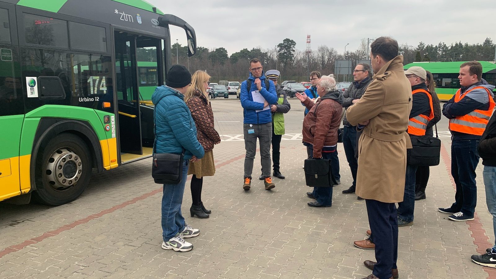 Na placu poznańskiego MPK stoi grupa osób i ogląda autobus w kolorze zielono-żółtym