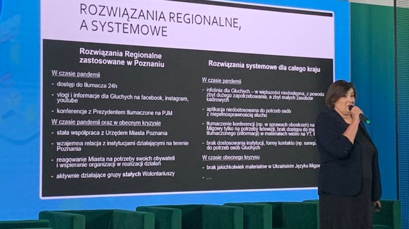 Przed ekranem stoi kobieta ubrana na czarno, mówi do mikrofonu. Na ekranie tytuł Rozwiązania regionalne a systemowe. - grafika artykułu