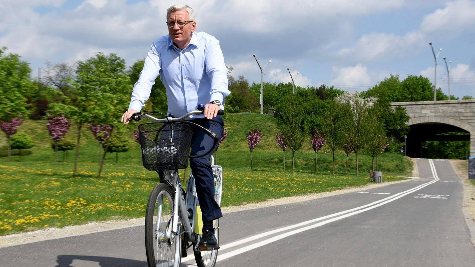 Jacek Jaśkowiak, prezydent Poznania na rowerze. W tle wiadukt i zieleń. - grafika artykułu
