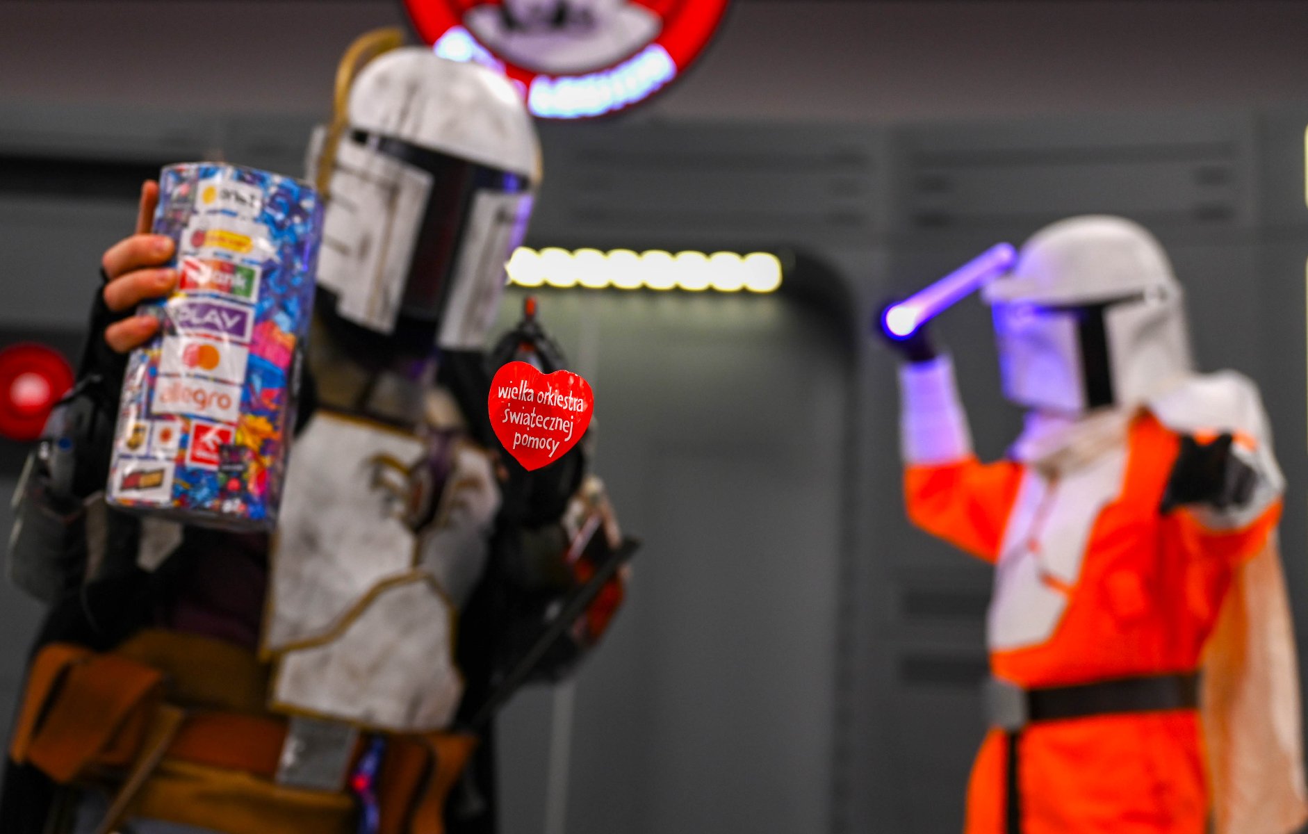 Na pierwszym planie widać czerwone serduszko WOŚP. W tle stoją dwie postaci w strojach z Gwiezdnych wojen