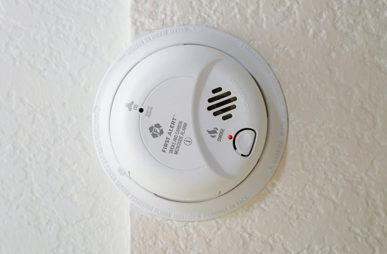 Na zdjęciu biała, okrągła czujka przymocowana do białej ściany