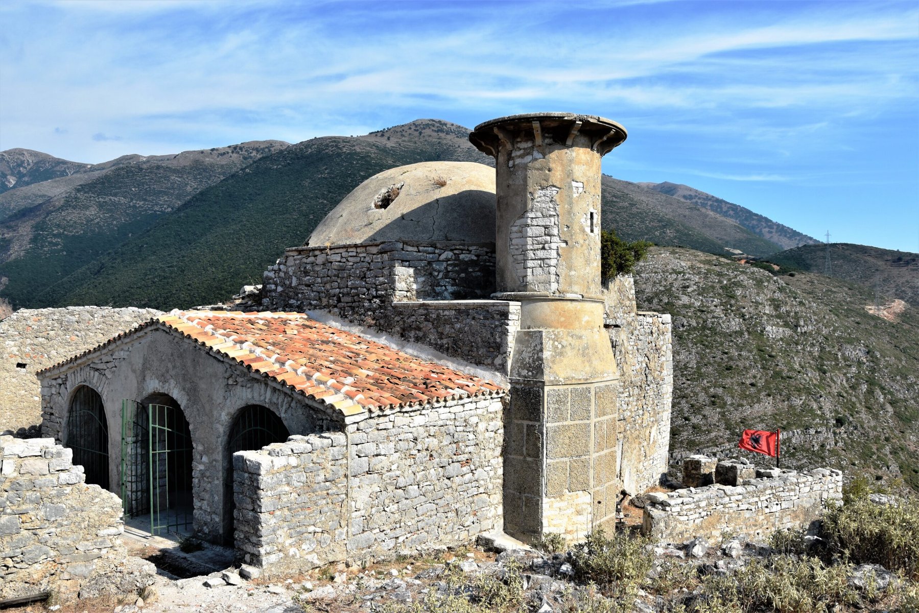 Na zdjęciu budowla wśród gór, na niej widać flagę Albanii