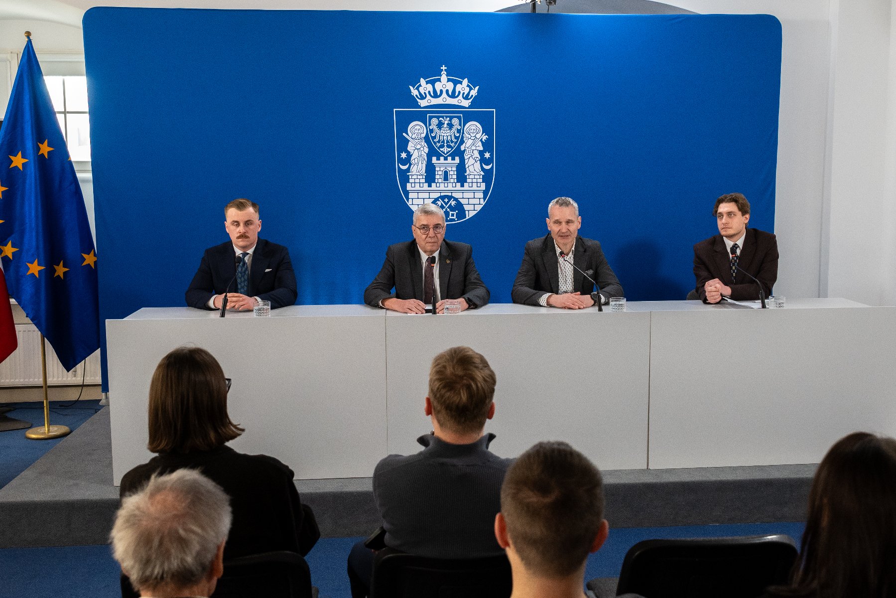 Na zdjęciu czterej mężczyźni siedzący za stołem konferencyjnym, w tle ścianka z herbem miasta