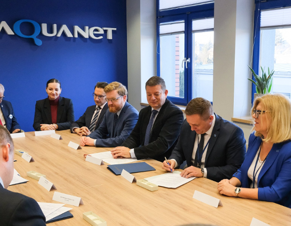 Na zdjęciu grupa ludzi przy stołach podpisujących dokumenty