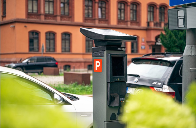 Aby skorzystać z niższych stawek za parkowanie, trzeba przede wszystkim potwierdzić fakt rozliczania podatku w Poznaniu Na zdjęciu parkomat, w tle czerwony, zabytkowy budynek