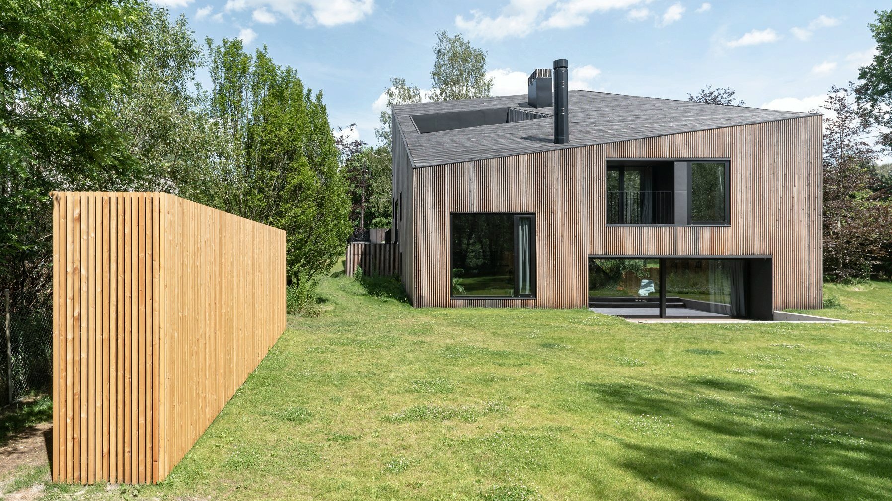 Zdjęcie przedstawia "Złamany Dom" - jego elewację tworzą drewniane deski. Przed budynkiem widać ogród z równo skoszoną trawą.