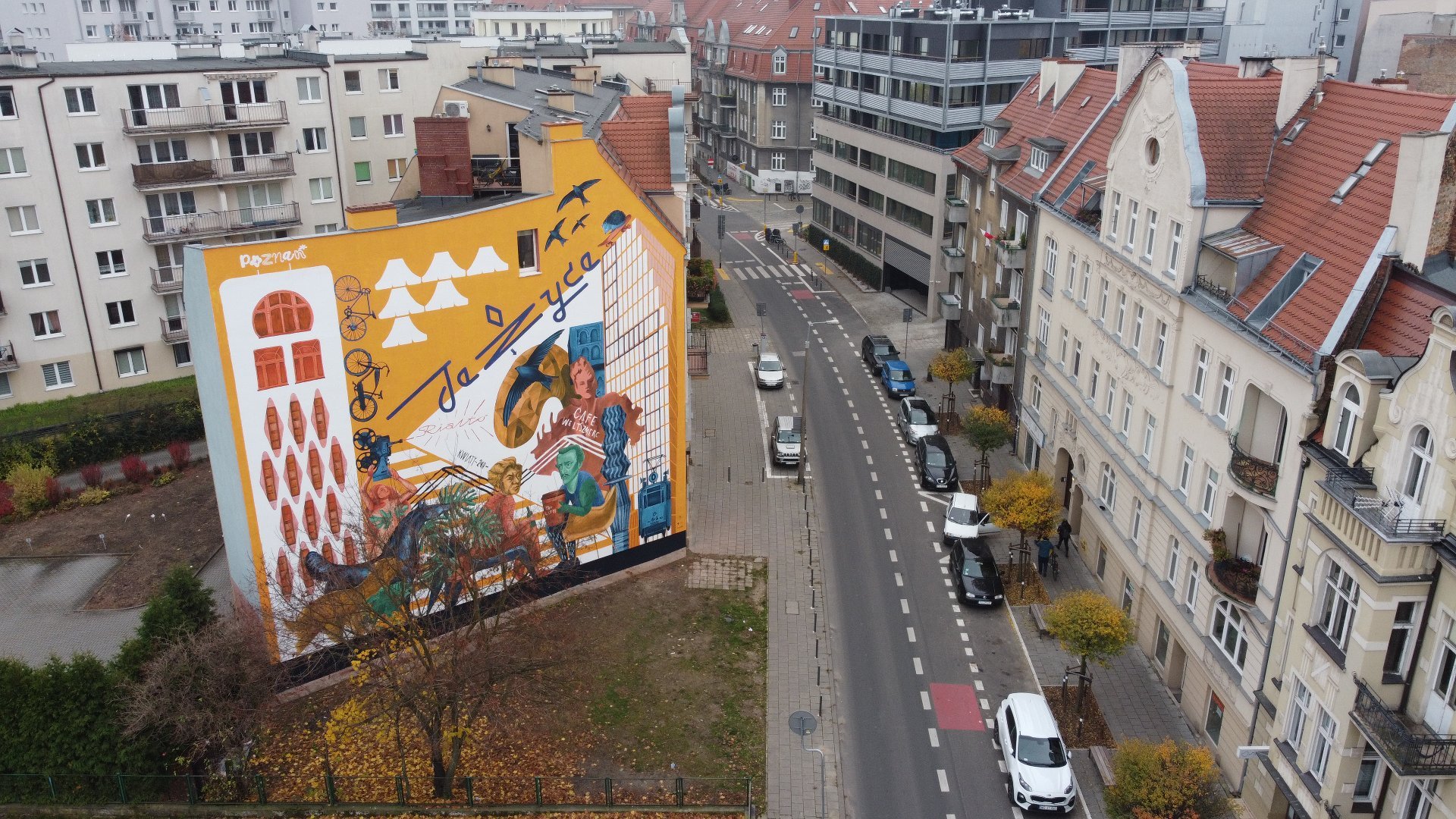 Galeria zdjęć przedstawia nowy mural na Jeżycach. Widać na nim m.in. dwóch poetów Słowackiego i Mickiewicza. Obok znajduje się ulica z samochodami.