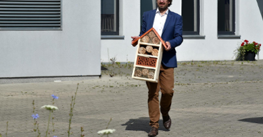 Krzysztof Albiński, dyrektor POSUM, niesie w ręku dom dla owadów. W tle - budynek POSUM.