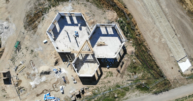 Na zdjęciu znajduje się plac budowy uwieczniony z góry przy pomocy drona. Widać na nim powstający dom działkowca, a także m.in. samochody dostawcze i materiały budowlane
