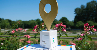 Na zdjęciu znajduje się nagroda Google - Złota Pinezka - uwieczniona na tle kwiatów w Parku Cytadela
