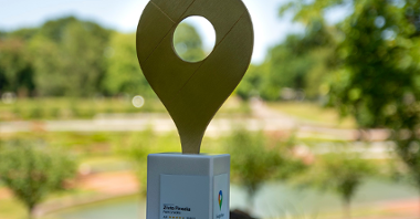 Na zdjęciu znajduje się nagroda Google - Złota Pinezka - uwieczniona na tle kwiatów, drzew i krzewów w Parku Cytadela