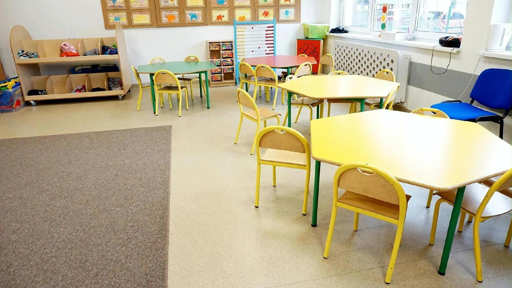 Sala lekcyjna/świetlica. Pod ścianami kolorowe stoły dla dzieci, wokół nich krzesła, w tle liczydło - grafika artykułu
