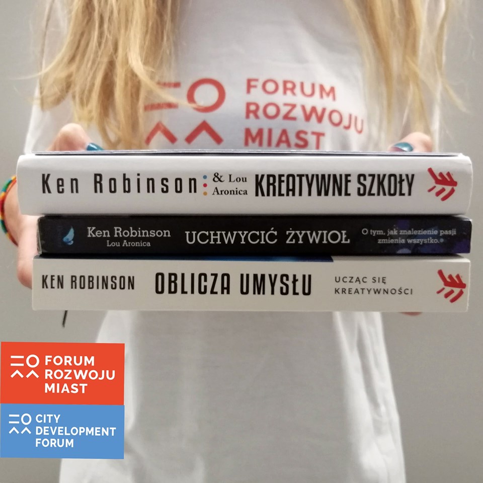 Kobieta trzymająca przed sobą trzy książki autorstwa Kena Robinsona - nie widać jej twarzy. Na bluzce ma napis: Forum Rozwoju Miast - grafika artykułu