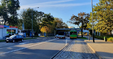Autobus wyjeżdża z przystanku na nowy buspas. Po obu stronach drzewa, a w tle most kolejowy