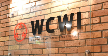 Zdjęcie przedstawia napis "WCWI" na szybie, wiszącej na ceglanej ścianie.