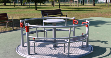 Zdjęcie przedstawia urządzenie na placu zabaw przeznaczone dla osób z niepełnosprawnościami (karuzela nie ma żadnego podwyższenia).