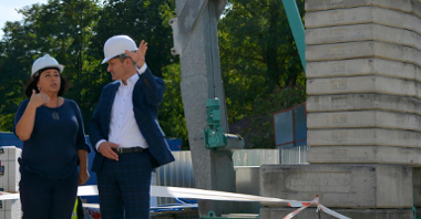 Po lewej stronie Jędrzej Solarski, zastępca prezydenta Poznania, rozmawia z kobietą na placu budowy. Oboje w kaskach, gestykulują. Po prawej materiały budowlane