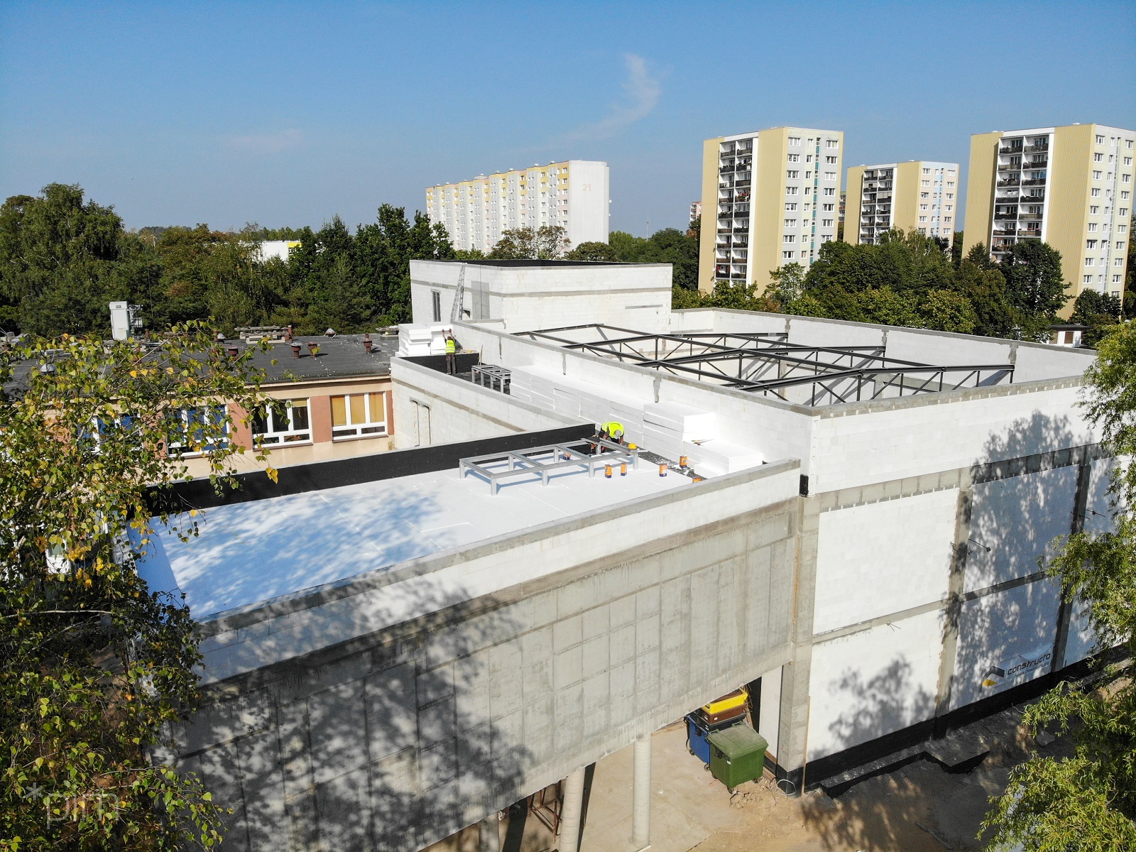 Zdjęcie przedstawia budynek szkoły w trakcie rozbudowy, widziany z góry. W tle znajdują się bloki. - grafika artykułu