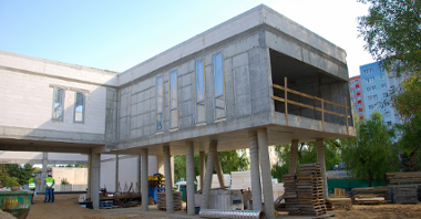 Zdjęcie przedstawia budynek szkoły w trakcie rozbudowy. Ten fragment budynku znajduje się na betonowych palach.