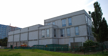 Zdjęcie przedstawia budynek szkoły w trakcie rozbudowy, widziany z góry. W tle, po lewej stronie znajdują się bloki.