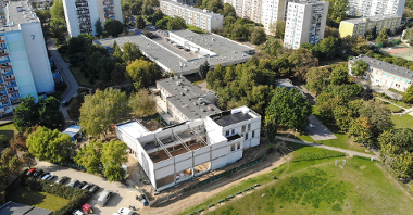 Zdjęcie przedstawia budynek szkoły w trakcie rozbudowy, widziany z góry. W tle znajdują się bloki.