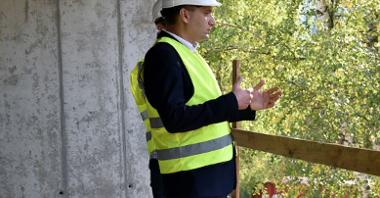 Zdjęcie przedstawia zastępcę prezydenta Poznania, Mariusza Wiśniewskiego, który spogląda z balkonu na teren zielony.