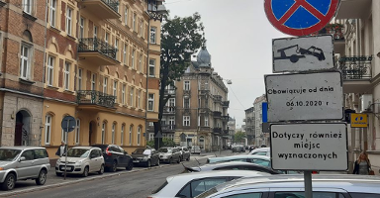 Znak przy ul. Małeckiego informujący o rozpoczęciu prac. Po obu stronach ulicy zaparkowane samochody