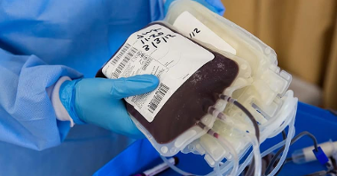 Na zdjęciu dłonie osoby w lekarskich rękawiczkach, trzymające worki z osoczem i krwią
