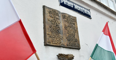 Na zdjęciu widać tablicę poświęconą pamięci Petera Mansfelda. Po bokach kadru flagi Poslki i Węgier.