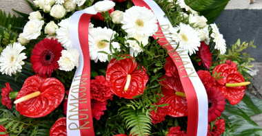 Na zdjęciu widać wieniec z białych i czerowonych kwiatów ze wstęgą z napisem "Romkowi, Poznaniacy"