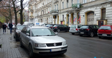 Ulica Łąkowa z zaparkowanymi samochodami i znakiem drogowym