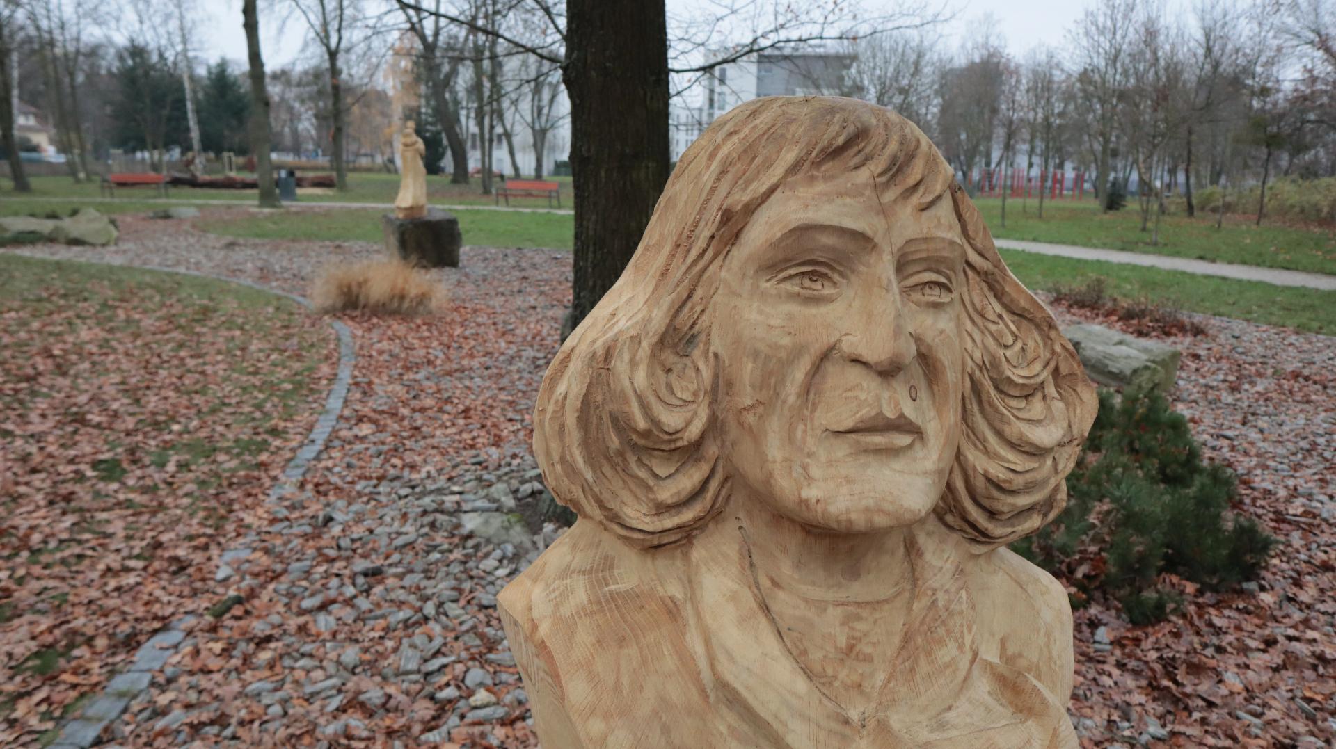 Zdjęcie przedstawia drewnianą rzeźbę Mikołaja Kopernika. W tle widać park oraz inną drewniana rzeźbę. - grafika artykułu