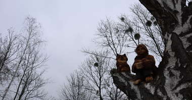 Zdjęcie przedstawia drewniane rzeźby Małego Księcia i lisa. Rzeźby umieszczoną na gałęzi drzewa.