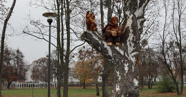 Zdjęcie przedstawia drewniane rzeźby Małego Księcia i lisa. Rzeźby umieszczoną na gałęzi drzewa.