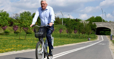 Jacek Jaśkowiak, prezydent Poznania na rowerze. W tle wiadukt i zieleń.