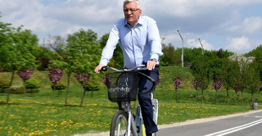 Jacek Jaśkowiak, prezydent Poznania na rowerze. W tle wiadukt i zieleń.