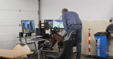 Zdjęcie przedstawia stymulator do nauki jazdy (trzy ekrany oraz kierownica). Przy urządzeniu siedzi uczeń, obok niego znajduje się nauczyciel.